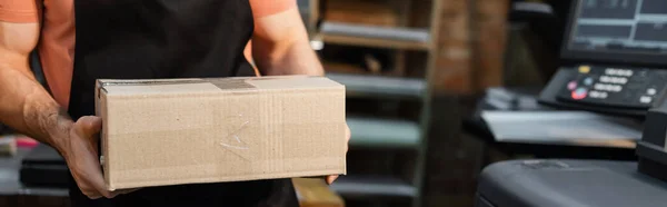 Обрізаний вид працівника в фартусі, що тримає картонну коробку в центрі друку, банер — стокове фото