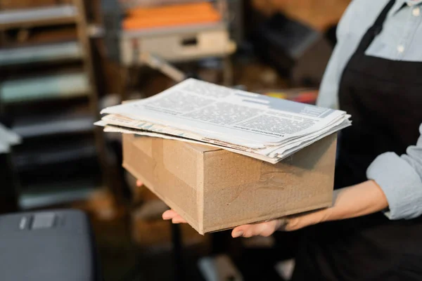 Vista parziale di tipografo donna in grembiule contenente scatola di cartone con giornali stampati — Foto stock
