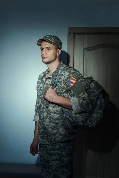 Displeased American soldier in camouflage standing in hallway at home at night — Stock Photo