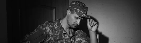 Photo en noir et blanc d'un soldat contrarié en uniforme debout dans un couloir à la maison la nuit, bannière — Photo de stock