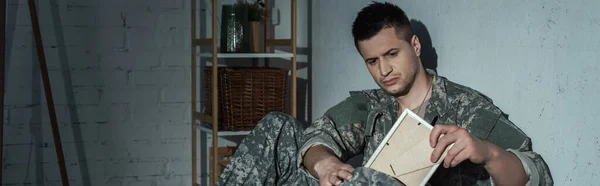 Soldat en uniforme prenant un cadre photo du sac à dos alors qu'il souffrait de détresse émotionnelle à la maison la nuit, bannière — Photo de stock