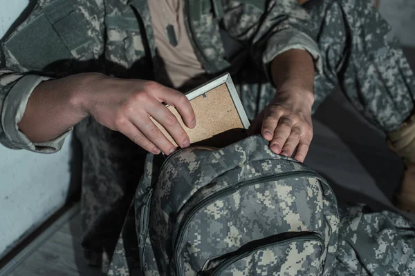 Обрезанный вид солдата с психическими проблемами, принимающего фоторамку из рюкзака дома ночью — стоковое фото