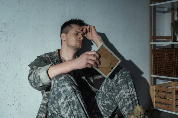 Veterano militar con angustia emocional sosteniendo el marco fotográfico en casa por la noche - foto de stock