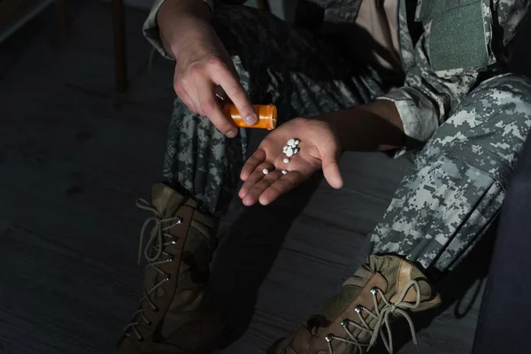 Cropped view of military veteran pouring pills on hand while suffering from emotional distress at home at night — Stock Photo