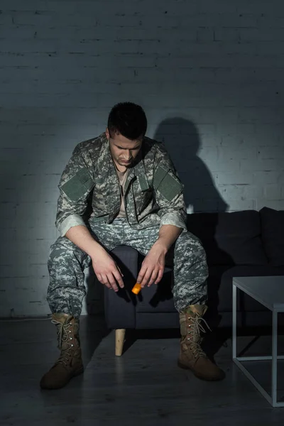 Soldat in Uniform hält Antidepressiva in der Hand, während er nachts zu Hause unter emotionalen Nöten leidet — Stockfoto