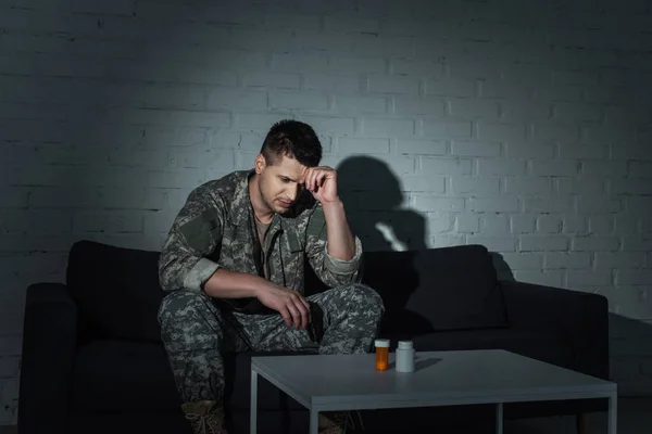 Veterano militar frustrado con ptsd mirando píldoras en la mesa por la noche - foto de stock