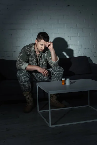 Soldado frustrado en uniforme sentado cerca de antidepresivos en casa por la noche - foto de stock