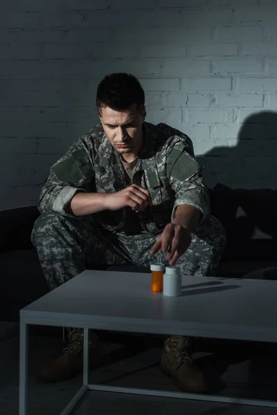 Депрессивный солдат в форме принимает таблетки от ptsd, сидя дома по ночам — стоковое фото