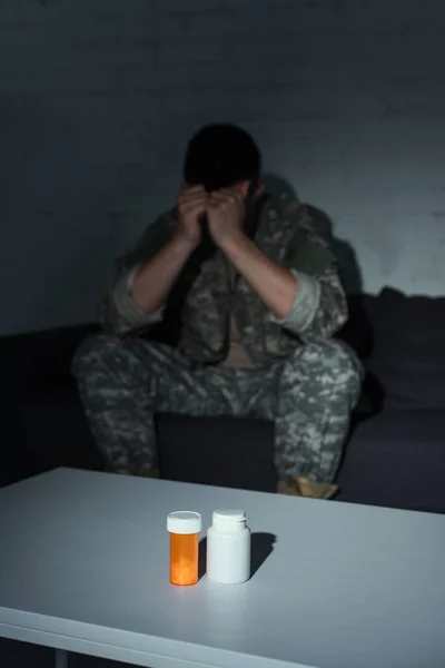 Таблетки на столе рядом с размытым ветераном войны с посттравматическим стрессовым расстройством дома ночью — стоковое фото