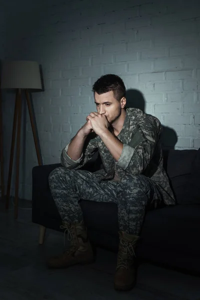 Soldado frustrado en camuflaje sentado en el sofá y sufriendo de ptsd en casa - foto de stock