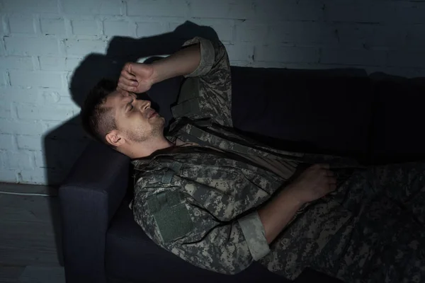 Depressed military man in uniform suffering from post traumatic stress disorder while lying on couch — Stock Photo