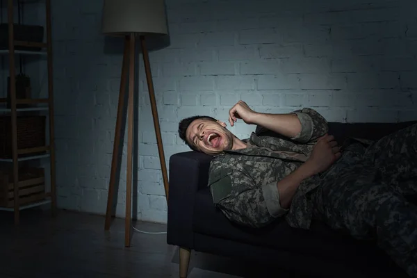 Stressed military man screaming while suffering from post traumatic stress disorder at home at night — Stock Photo