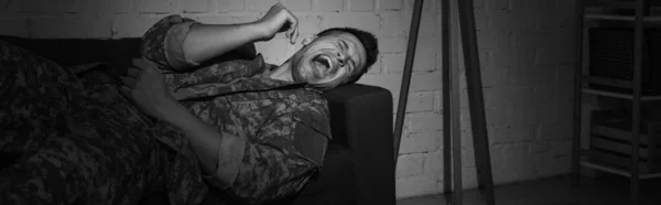 Black and white photo of anxious serviceman screaming while suffering from post traumatic stress disorder, banner — Stock Photo