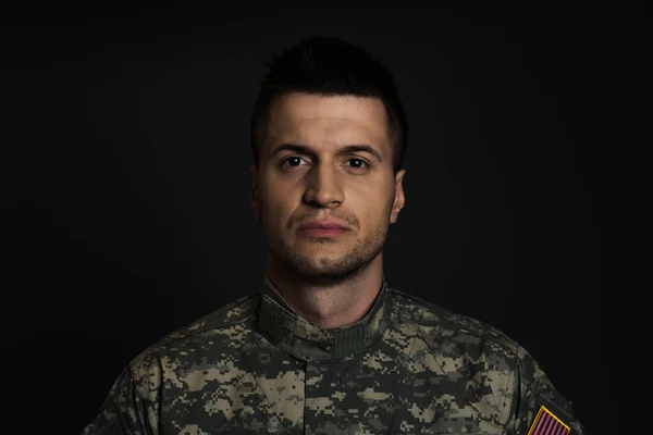 Joven militar en uniforme que sufre de ptsd y mirando a la cámara aislada en negro - foto de stock