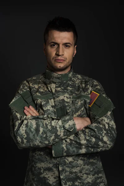 Soldat américain déprimé en uniforme debout avec les bras croisés isolés sur noir — Photo de stock