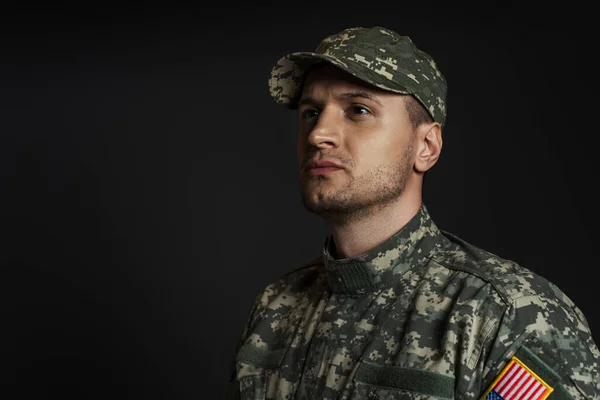 Soldat patriotique en uniforme avec drapeau américain regardant loin isolé sur noir — Photo de stock