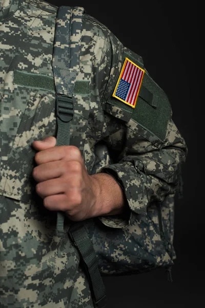 Cropped view of American serviceman in military uniform with flag standing with backpack isolated on black — Stock Photo