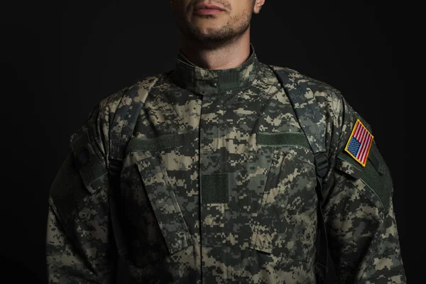 Cropped view of patriotic American serviceman in military uniform with flag standing  isolated on black — Stock Photo