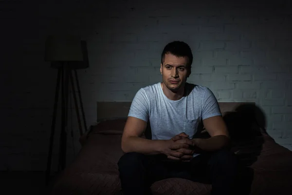Depressiver Mann im weißen T-Shirt sitzt auf dem Bett, während er an ptsd leidet — Stockfoto