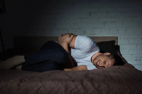 Молодой человек с закрытыми глазами, страдающий посттравматическим стрессовым расстройством, лежа ночью на кровати — стоковое фото