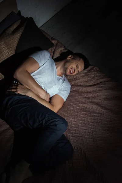 Vista superior del hombre deprimido con los ojos cerrados que sufren de trastorno de estrés postraumático mientras está acostado en la cama por la noche - foto de stock