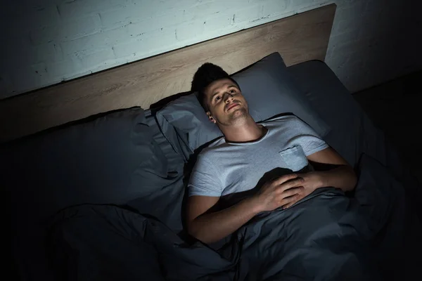 Вид сверху проснувшегося молодого человека с ptsd, лежащего на кровати и страдающего хроническим алкоголизмом по ночам — стоковое фото