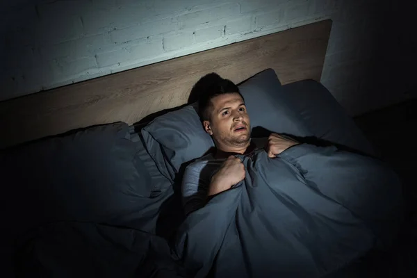 Vista superior do homem assustado que sofre de ataques de pânico e ter insônia enquanto deitado sob cobertor — Fotografia de Stock