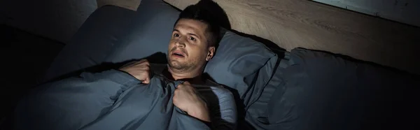 Von oben: verängstigter Mann, der unter Panikattacken leidet und Schlaflosigkeit hat, während er unter Decke liegt, Banner — Stockfoto