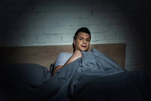 Стресовий чоловік з панічними атаками, що мають безсоння, лежачи під ковдрою — стокове фото