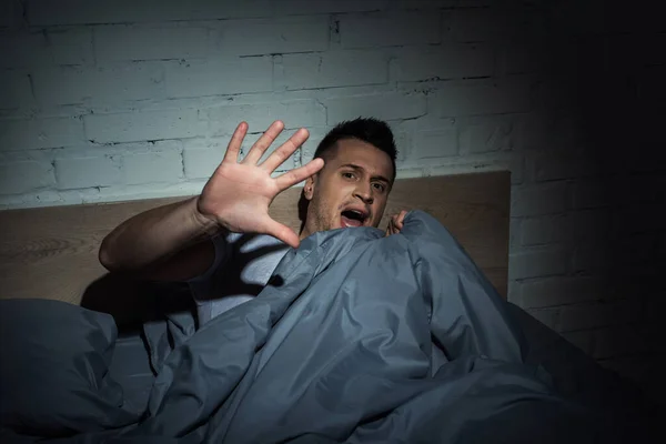 Uomo spaventato con attacchi di panico urlando mentre giaceva sotto la coperta — Foto stock