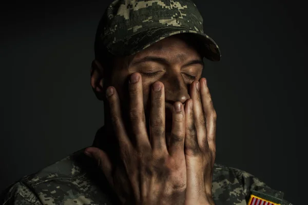 Militar con los ojos cerrados cubriendo la cara con las manos sucias y sufriendo de ptsd aislado en gris - foto de stock
