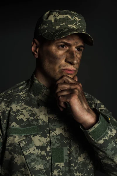 Вдумчивый военнослужащий, касающийся подбородка грязной рукой, глядя в сторону, изолированную от серого — стоковое фото