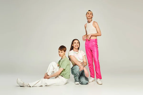 Diverse group of cheerful young lgbt community people in colorful clothes smiling while sitting together and celebrating pride day on grey background in studio — Stock Photo