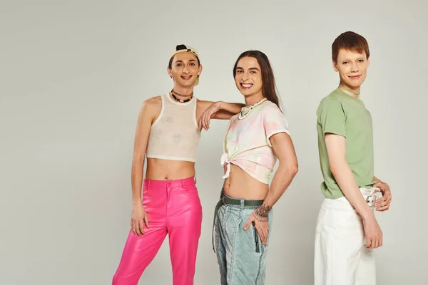 Diverse and young lgbtq community friends with tattoos standing in colorful clothes smiling while looking at camera in studio on pride month, grey background — Stock Photo