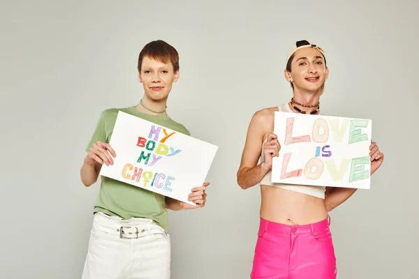 Glücklich schwule Männer halten Plakate mit meinem Körper meine Wahl und Liebe ist Liebe Schriftzug, während zusammen stehen und in die Kamera auf Stolz Monat, grauer Hintergrund — Stockfoto