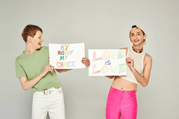 Happy lgbt friends holding placards with love is love and my body my choice lettering while standing together on pride month, grey background — Stock Photo