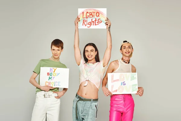 Happy lgbt friends holding placards with my body my choice, lgbtq rights and love is love lettering while standing together on pride month, grey background — Stock Photo