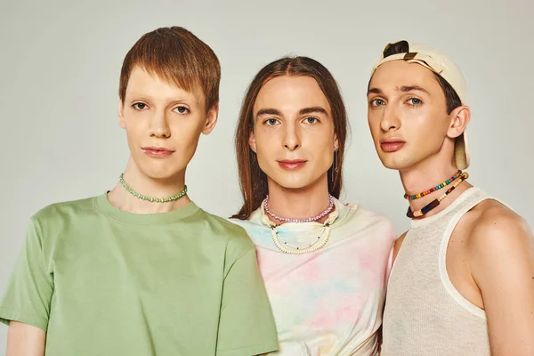 Portrait de trois personnes lgbtq avec des perles colorées regardant la caméra tout en se tenant ensemble sur fond gris en studio, célébration du concept du mois de la fierté — Photo de stock