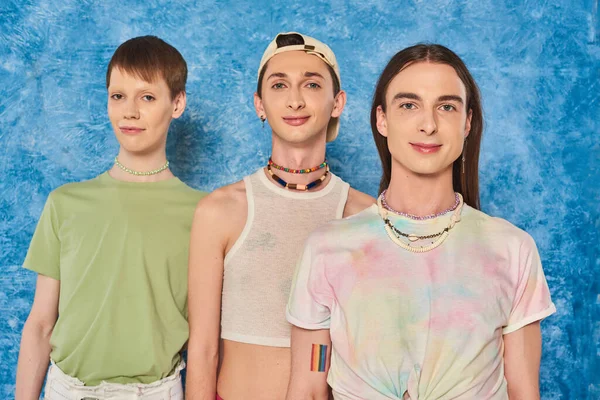 Портрет молодого и стильного гомосексуального сообщества, смотрящего в камеру во время празднования месяца гордости на пестром и текстурированном синем фоне — стоковое фото