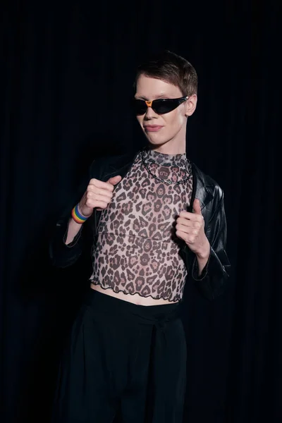 Модный гомосексуалист в блузке с отпечатками животных и солнцезащитными очками позирует во время месячной вечеринки сообщества lgbt, изолированной на черном — стоковое фото