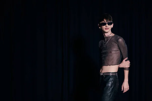 Trendiger junger schwuler Mann mit Sonnenbrille, funkelndem Top und Lederhose posiert, während er lgbt Community und Stolz Monat isoliert auf schwarz feiert — Stockfoto