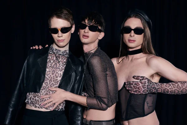 Fashionable young and homosexual friends in sunglasses and party outfits posing during lgbt community and pride month isolated on black — Stock Photo