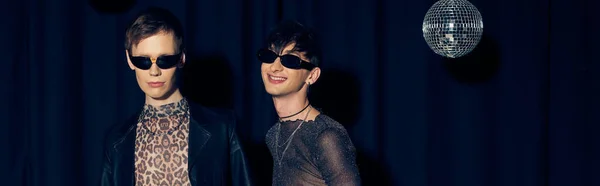 Lächelnde und trendige junge queere Freunde in Sonnenbrille neben Discokugel bei Party und Pride-Monatsfeier auf schwarzem Hintergrund, Banner — Stockfoto