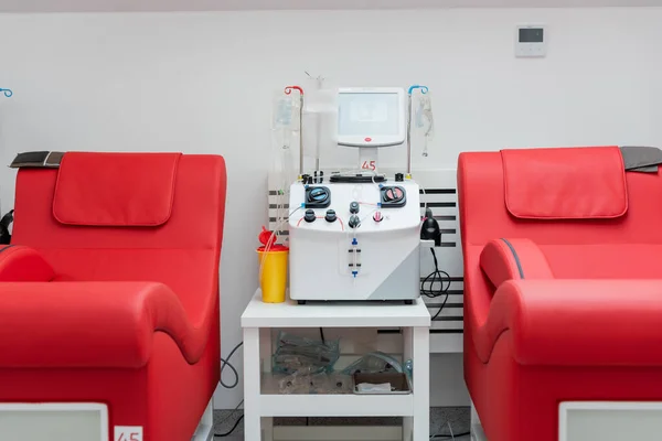 Медицинские стулья с удобной эргономичной конструкцией рядом с автоматизированной машиной для переливания крови, сенсорным экраном, пластиковыми чашками и капельницами с инфузионными пакетами в центре донорства крови — стоковое фото