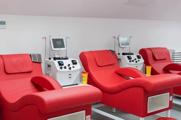 Cómodas sillas médicas con diseño ergonómico cerca de vasos de plástico y máquinas automatizadas de transfusión con pantallas táctiles en el ambiente estéril del centro de donación de sangre — Stock Photo