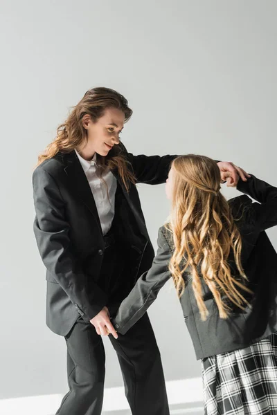 Модна мати і дочка, жінка в костюмі тримає руки зі школяркою в шкільній формі з плетеною спідницею, блейзерами, бізнес-леді, готується до нового шкільного року, розважається — стокове фото