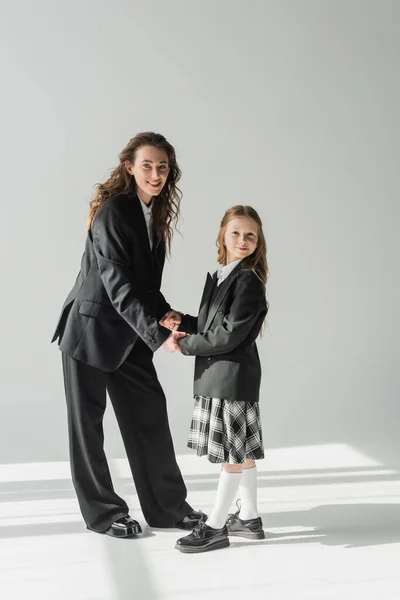 Mother and daughter, happy woman in suit holding hands with schoolgirl in school uniform with plaid skirt, businesswoman, blazers, getting ready for new school year, looking at camera — Stock Photo