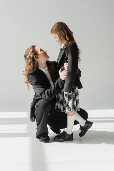 Modern mother and daughter, businesswoman in suit hugging schoolgirl in uniform with plaid skirt, blazers, getting ready for new school year, encouraging, looking at each other — Stock Photo