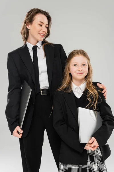 Mãe e filha, nomadismo digital, trabalho remoto, e aprendizagem, empresária de terno e menina em pé junto com laptops em fundo cinza no estúdio, ligação, parentalidade moderna — Fotografia de Stock