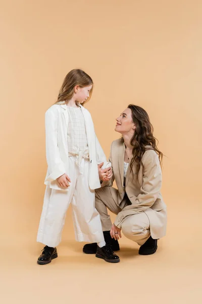 Stilvolle Mutter und Tochter in Anzügen, Frau und Mädchen, die sich anschauen, während sie zusammen auf beigem Hintergrund stehen, modische Outfits, formelle Kleidung, Corporate Mom, moderne Familie — Stockfoto